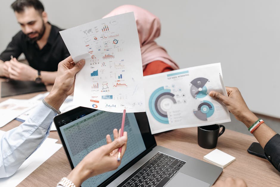 Team analyzing graphs and data during a business meeting, showcasing hands-on engagement with paperwork and laptops.