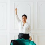 Confident woman in white blouse celebrating success with raised arm indoors.