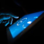 Close-up of a hand interacting with a glowing touchscreen in a dark setting, highlighting technology use.