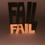 Wooden blocks spelling 'FAIL' casting a dramatic shadow against a brown background in a studio setup.