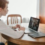 Young man engaged in a video call on a laptop at home, indicating remote communication.